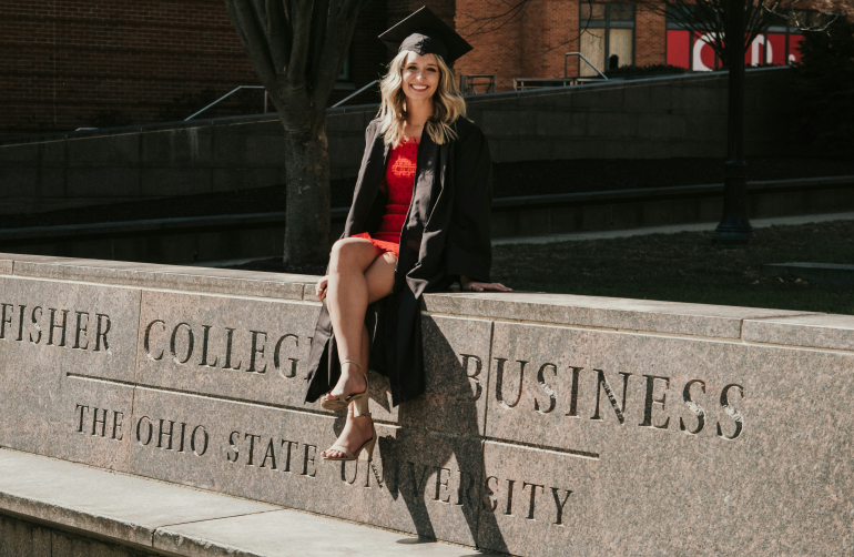 a woman in a graduation gown sitting on a stone wall