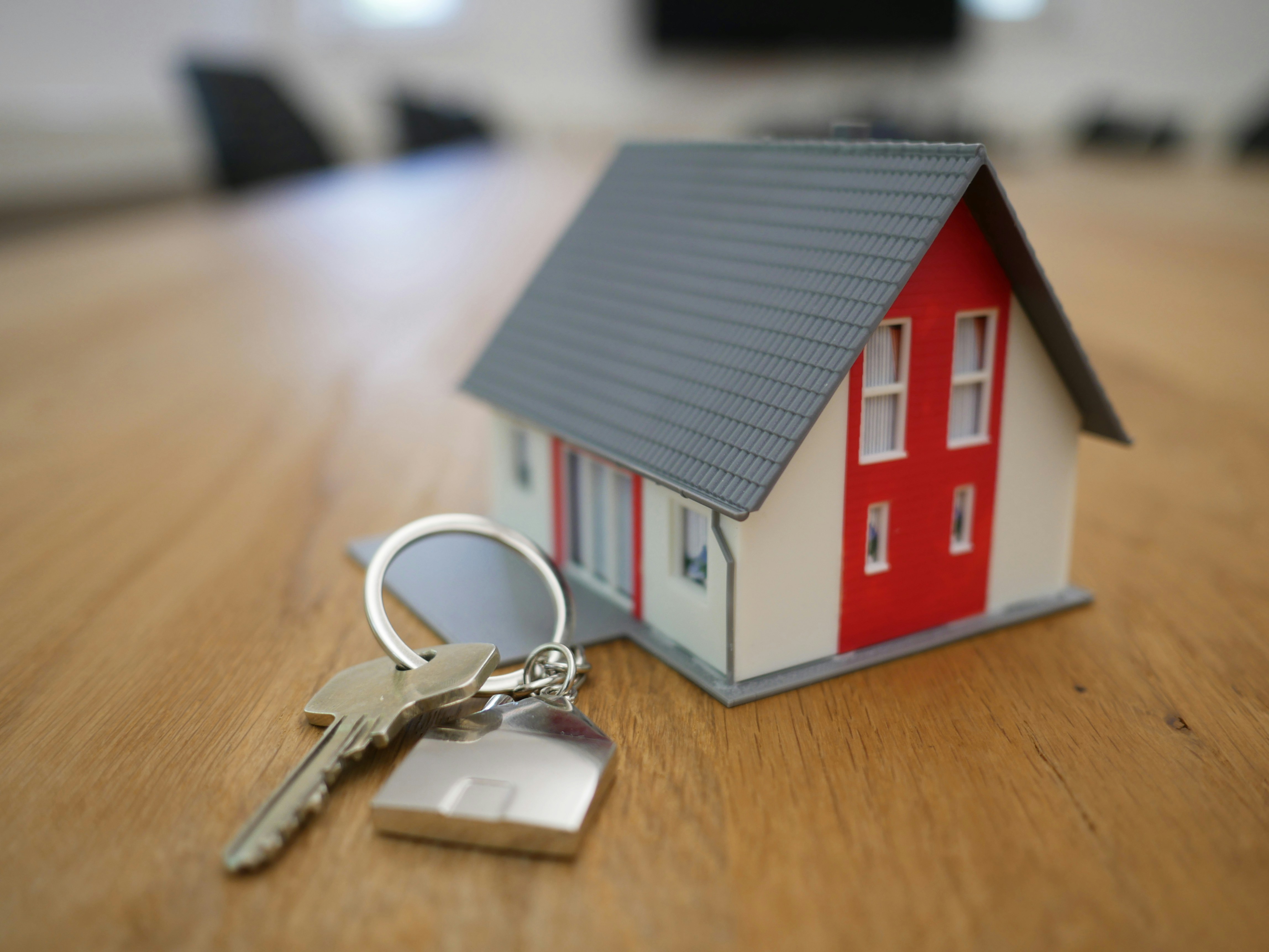 a white and red wooden house miniature and keys on a brown table