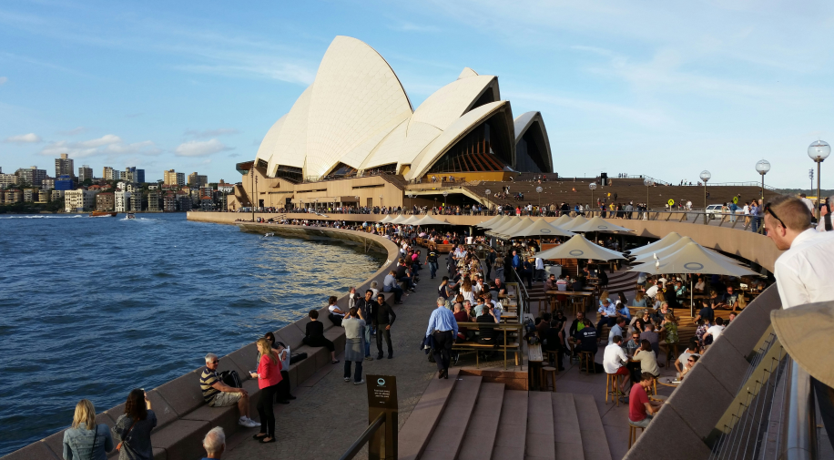 people walking on a beach besides sydney opera