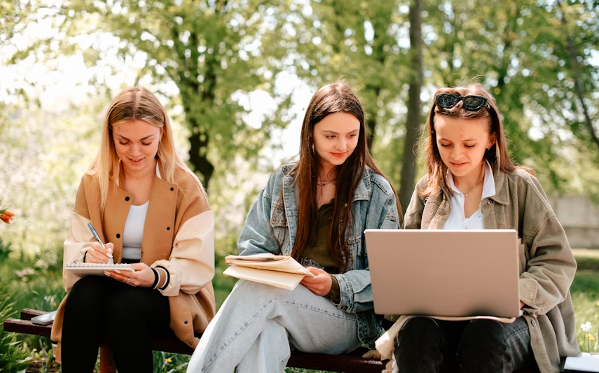three girls sitting on a bench and looking at a laptop