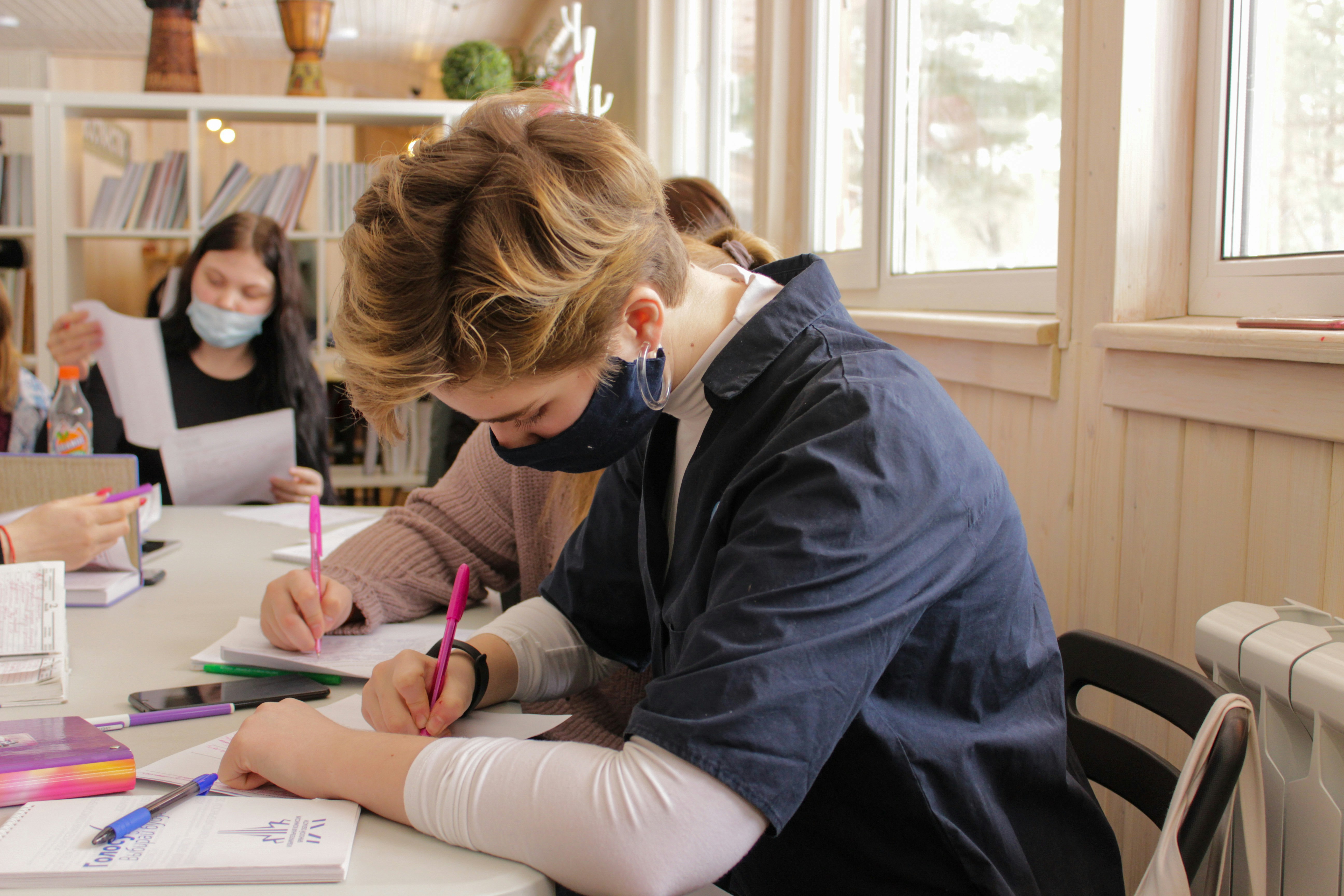 a woman in a blue long sleeve shirt writing on a paper