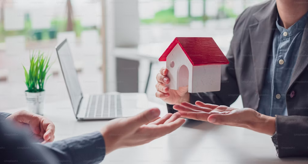 a man holding a house model talking to another man