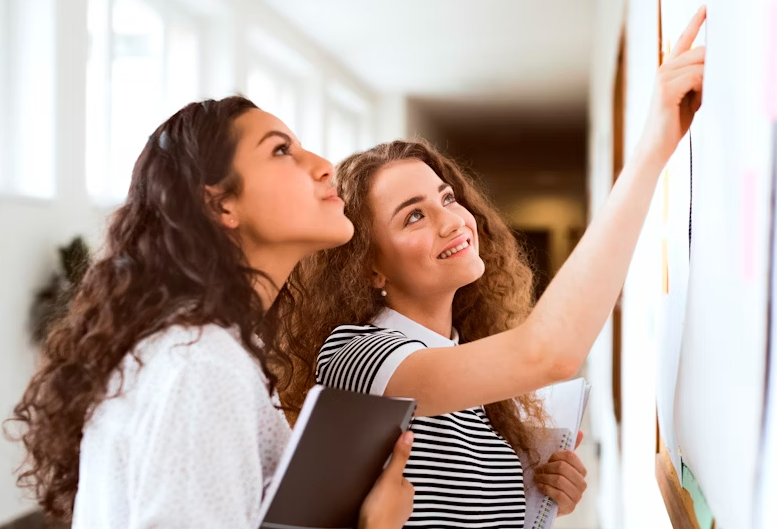 tow high school girls reading something on notice board