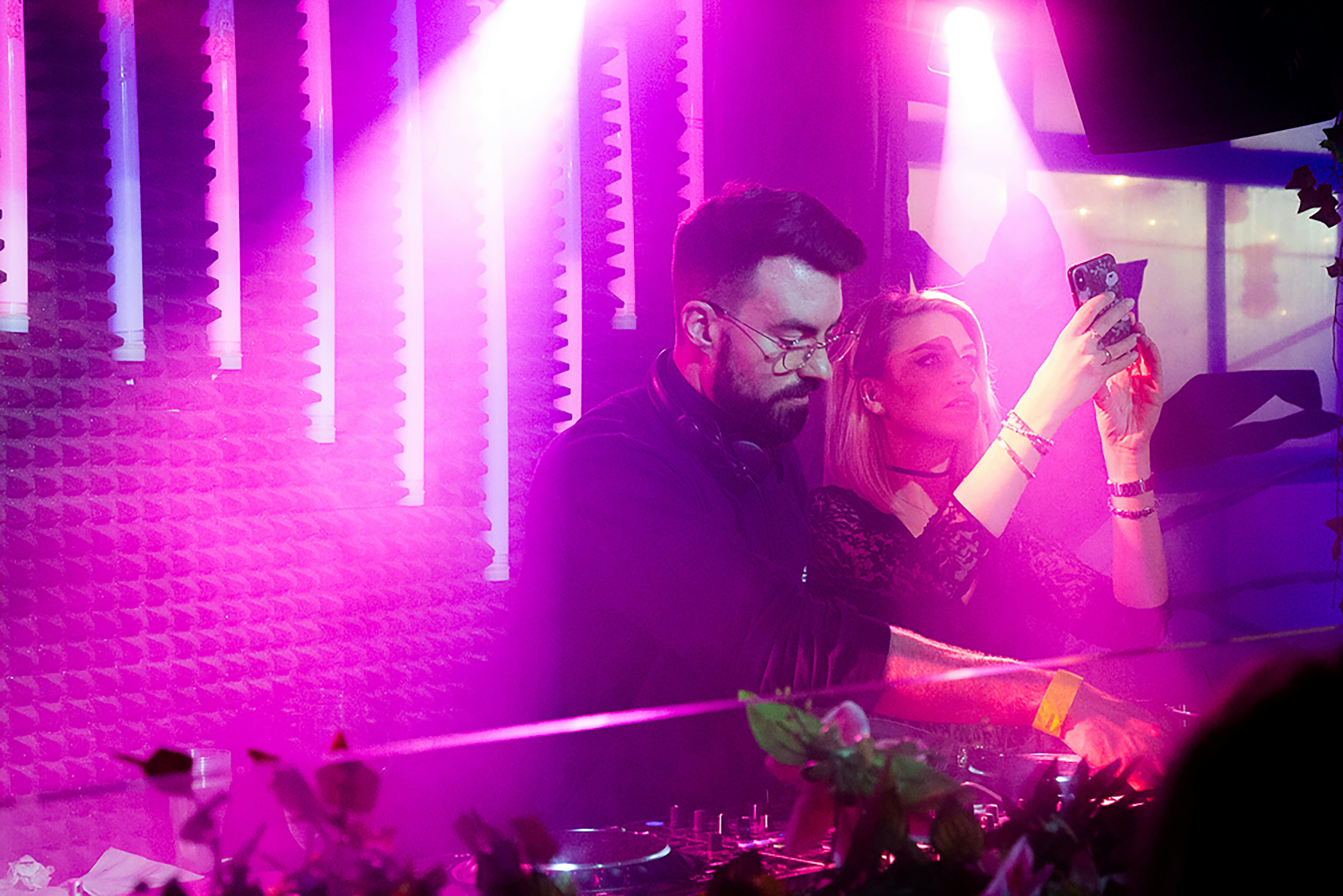 a male DJ with a woman in the back in club in London