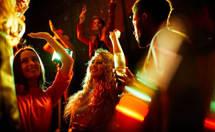 girls dancing in a club and talking with a man holding a glass of wine
