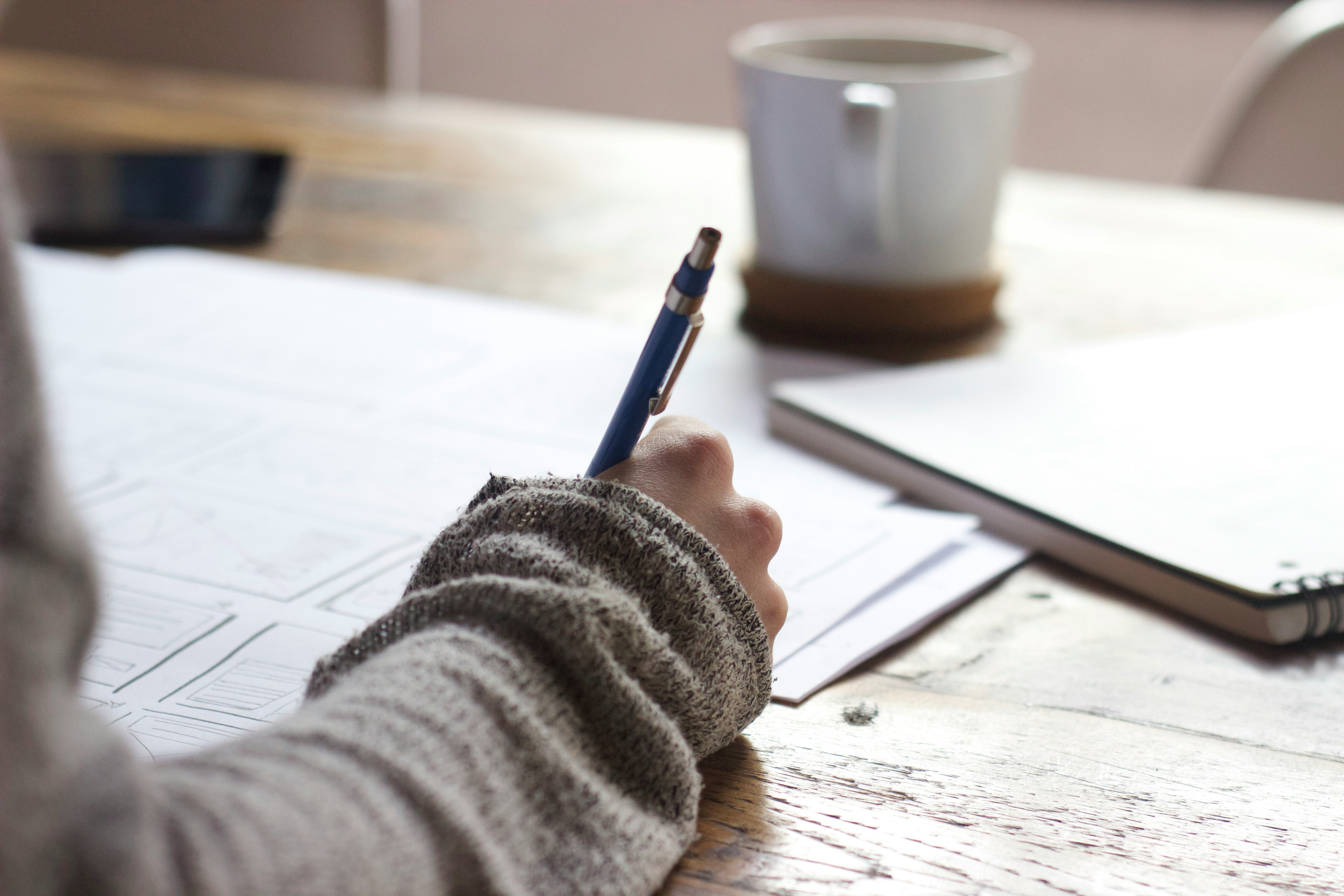 woman writing on a brown table beside a white mug